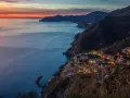 Riomaggiore cosa vedere: un villaggio colorato aggrappato alla scogliera, illuminato al tramonto, con il mare blu e le montagne sullo sfondo.
