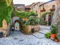 Un vicolo acciottolato tra antiche case in pietra, ricoperte di edera e fiori. Un invito a scoprire i borghi da visitare nelle Marche.