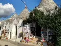 Trulli caratteristici della Valle d'Itria cosa vedere: negozi di souvenir con prodotti locali e decorazioni tipiche sotto un cielo azzurro.