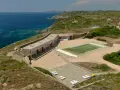 Un villaggio nurra affacciato sul mare turchese, con una piscina e lettini bianchi pronti per il relax.