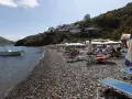 Spiaggia di ciottoli a Lipari, con lettini, ombrelloni e una barca all'ancora. La papesca beach è un luogo ideale per rilassarsi.