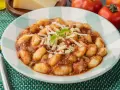 Gnocchi al ragù, un classico tra i piatti tipici di Perugia, serviti con parmigiano grattugiato e basilico fresco.