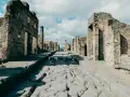 Antica strada romana a Pompei, con rovine di edifici e turisti che passeggiano. Un'ottima guida per come visitare Pompei.