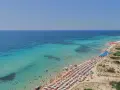 Spiaggia affollata con ombrelloni colorati e gente che nuota nelle acque cristalline di Punta Prosciutto, le Maldive del Salento.