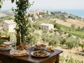 Un pranzo all'aperto nelle Marche: pasta, arrosti, fritti e pesce con vista su colline e borghi.
