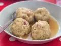 Canederli in brodo, un classico dei piatti tipici trentino alto adige, serviti in una ciotola bianca su un tovagliolo rosso a pois bianchi.