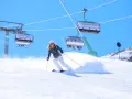 Donna scia su pendio innevato, con seggiovie sullo sfondo. Perfetta per la tua settimana bianca dove andare.