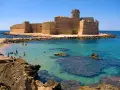 Castello Aragonese sull'acqua cristallina della costa ionica Calabria, con bagnanti che si godono il sole e il mare.