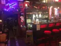 Interno della locanda del Principe a Artena, con chitarra elettrica luminosa, bancone bar e sgabelli rossi.