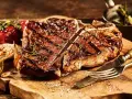 Una succulenta fiorentina, cotta alla perfezione, riposa su un tagliere di legno, pronta per essere gustata. Accanto, pomodorini e aglio arrostiti.