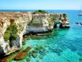Scogliere bianche e mare cristallino sul litorale adriatico. Turisti ammirano il panorama, un catamarano naviga in lontananza.
