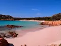 La **spiaggia rosa** di Asinara, con le sue acque turchesi e rocce rossastre, incanta sotto un cielo azzurro.