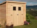 La casetta in campagna, in legno chiaro, con due finestrelle e un cesto di legna, si affaccia su un panorama collinare con un borgo in lontananza.