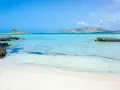 Spiagge di Alghero con torre antica su isolotto e acque cristalline turchesi.