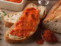 Fetta di pane con 'nduja, uno dei piatti tipici della Calabria, accanto a una ciotola con la crema e un cucchiaino di peperoncino in polvere.