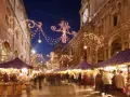 Una strada illuminata da lucine natalizie, con bancarelle e gente che passeggia: ecco i mercatini di Natale più belli.