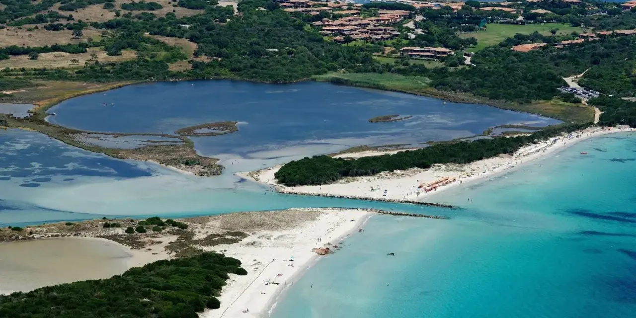 Vista aerea della spiaggia La Cinta con acque turchesi, lagune interne e vegetazione lussureggiante.