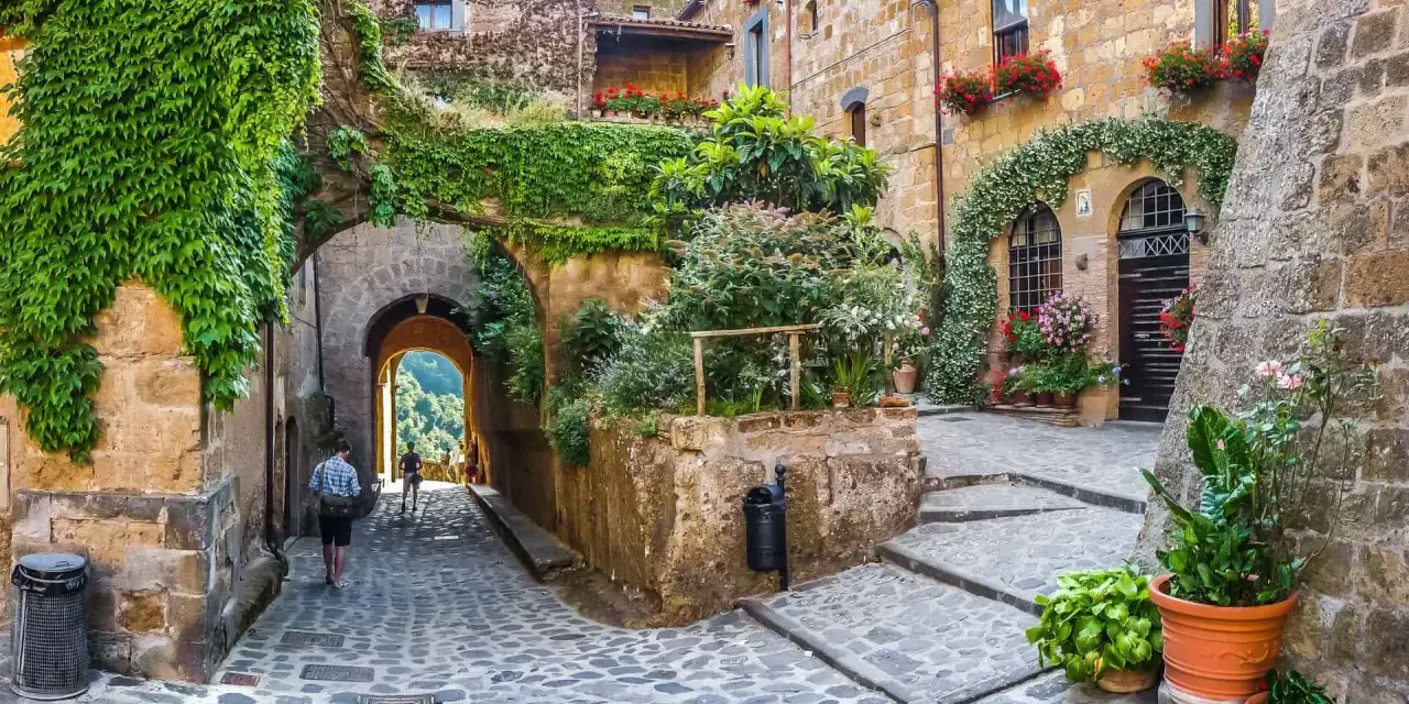 Un vicolo acciottolato tra antiche case in pietra, ricoperte di edera e fiori. Un invito a scoprire i borghi da visitare nelle Marche.