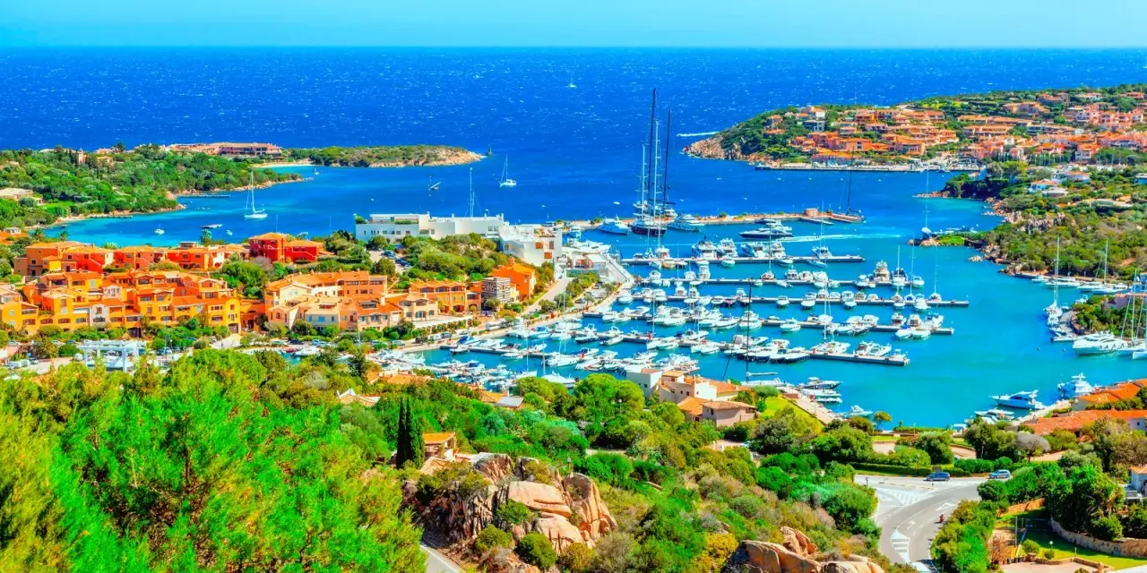 Vista panoramica di Porto Cervo con il suo porto turistico pieno di yacht e le case colorate che si affacciano sul mare cristallino. Un luogo da sogno per scoprire cosa vedere a Porto Cervo.
