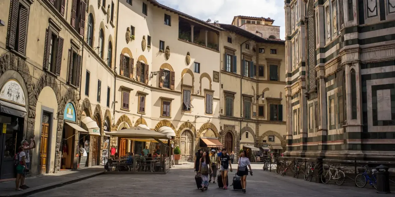Un gruppo di turisti con valigie a rotelle cammina in una piazza fiorentina, un'immagine perfetta per un **viaggio in Toscana**.