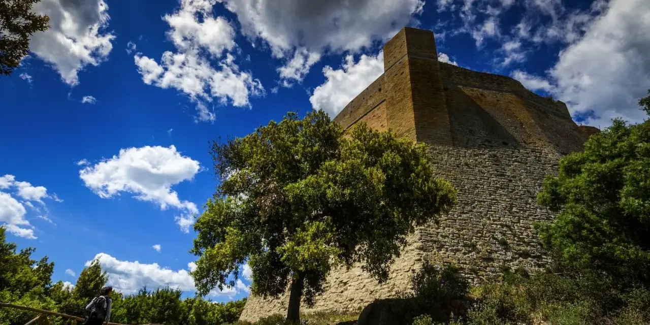 Roccia imponente e cielo azzurro con nuvole bianche: ecco cosa vedere a Pomarance, con un escursionista che ammira la fortezza.