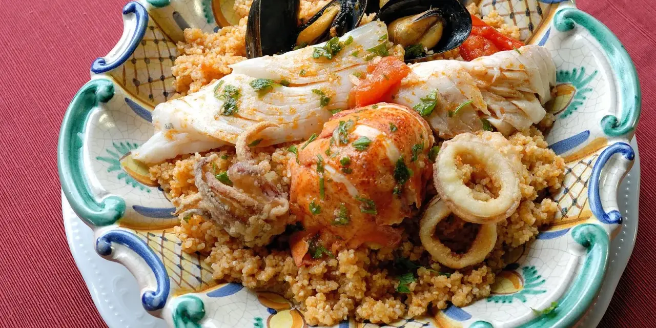 Piatto di pesce misto con couscous: ecco cosa mangiare a Trapani. Gamberi, calamari, pesce bianco e cozze.