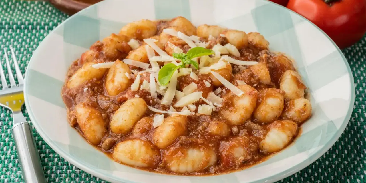 Gnocchi al ragù, un classico tra i piatti tipici di Perugia, serviti con parmigiano grattugiato e basilico fresco.