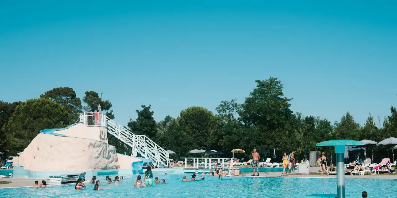 Bambini e adulti si divertono nella piscina del villaggio Ca' Laguna, con scivoli e zone relax sotto il sole.