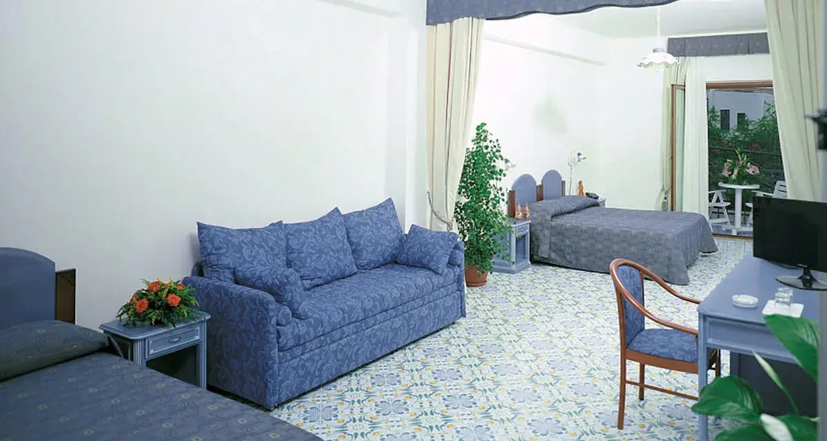 Camera spaziosa con divano blu, letti singoli e un letto matrimoniale. Pavimento decorato, tipico del **hotel club residence Martinica**.
