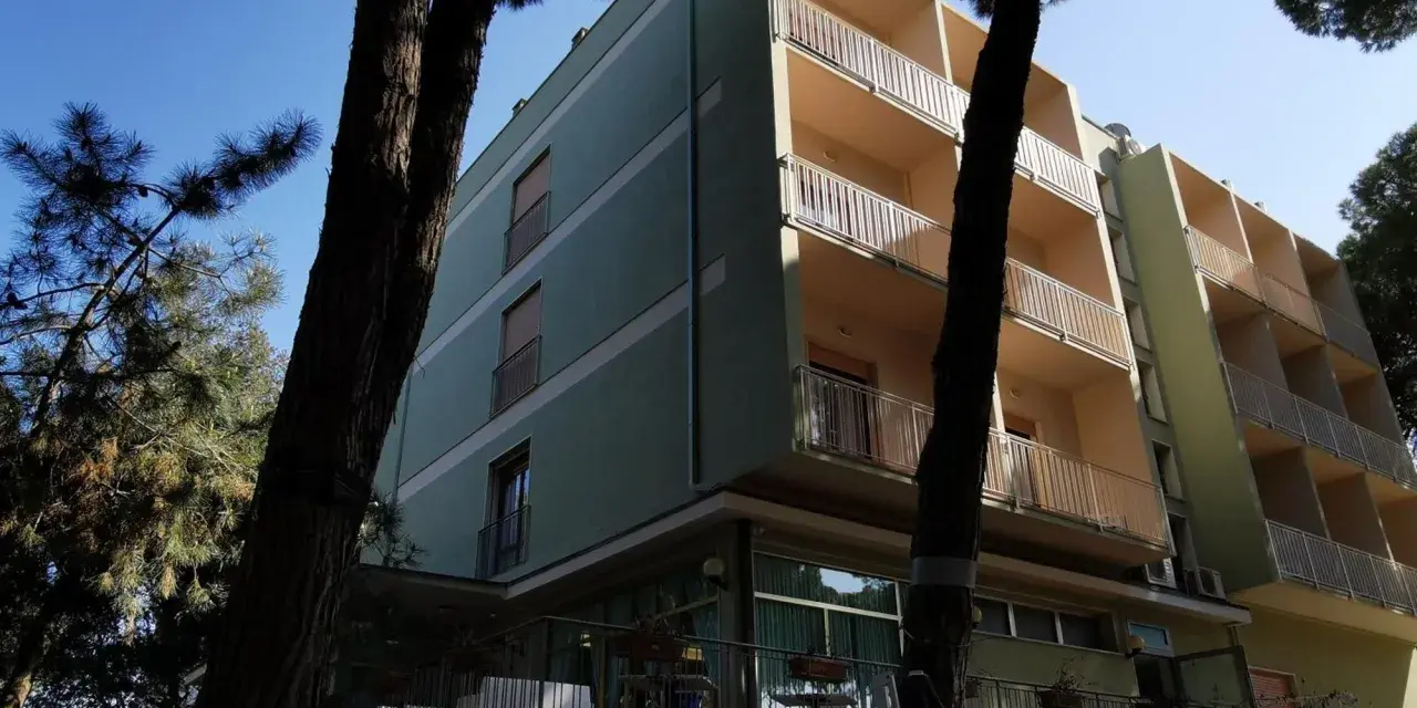 Edificio del pine beach hotel rosolina mare, con balconi e alberi di pino davanti.