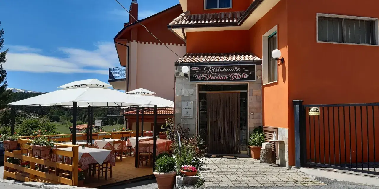 Ristorante La Vecchia Fonte, con tavoli all'aperto sotto ombrelloni bianchi, in una giornata di sole.