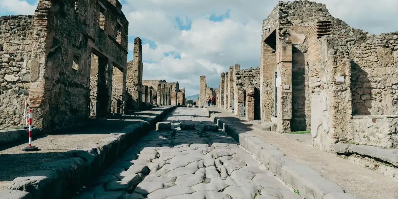 Antica strada romana a Pompei, con rovine di edifici e turisti che passeggiano. Un'ottima guida per come visitare Pompei.