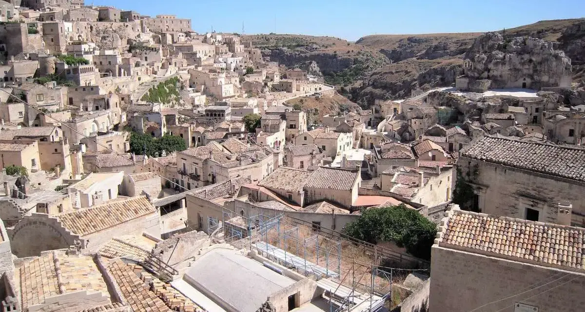 Panoramica dei Sassi di Matera, un **itinerario** suggestivo tra antiche case scavate nella roccia e tetti in cotto sotto un cielo azzurro.