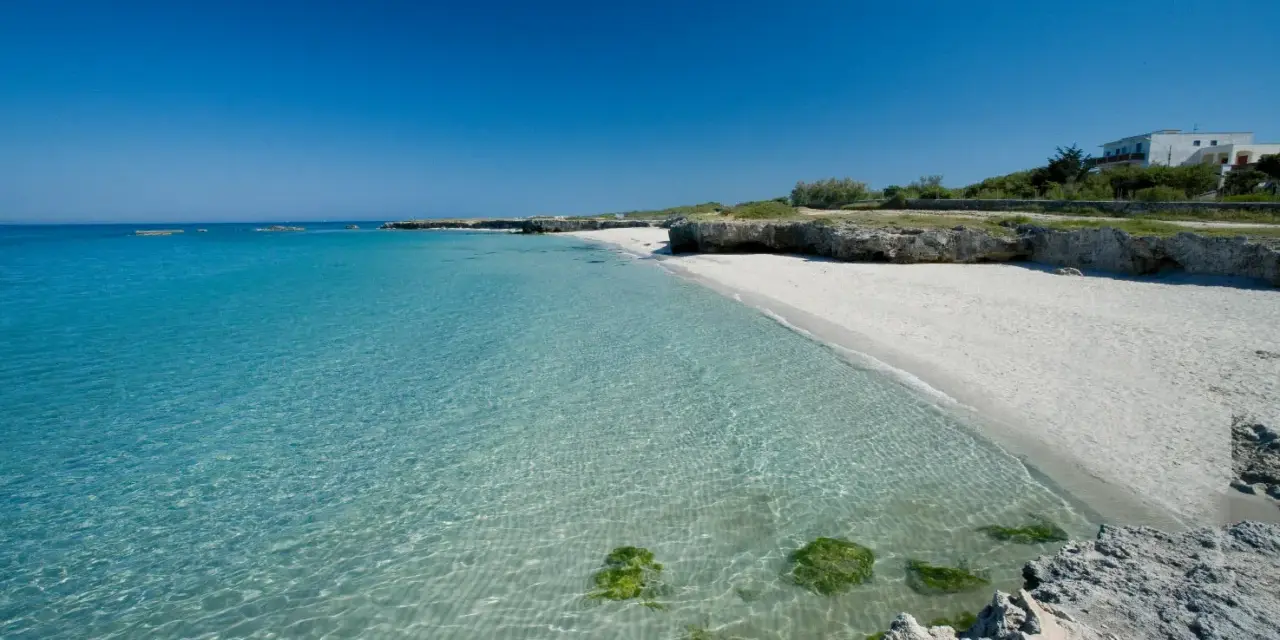Spiaggia bianca e mare cristallino in Puglia, con rocce e vegetazione. Un angolo di paradiso per godersi il sole e il **mare** della **Puglia**.