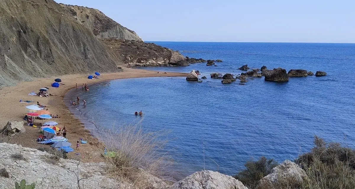 Spiaggia di Cala Vincenzina con scogliere, ombrelloni colorati e bagnanti che si godono il mare azzurro.