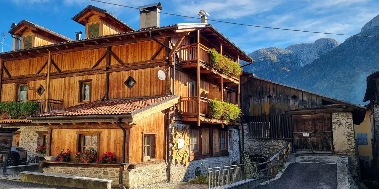 Casa in legno con balconi fioriti e montagne sullo sfondo. Un cartello "Alle Meridiane" indica un luogo incantevole a Lagopesole.
