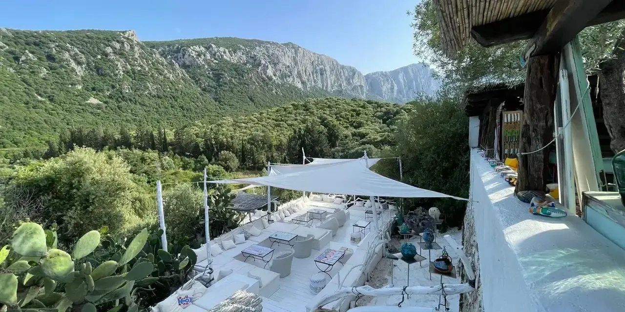 Terrazza panoramica con vista sui monti di Oliena, Sardegna. Arredamento bianco, cactus e vegetazione rigogliosa.