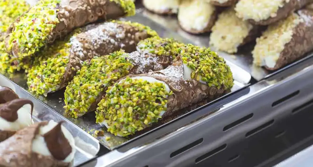 Cannoli siciliani, dolci tipici siciliani, ricoperti di pistacchi e zucchero a velo, in una vetrina.