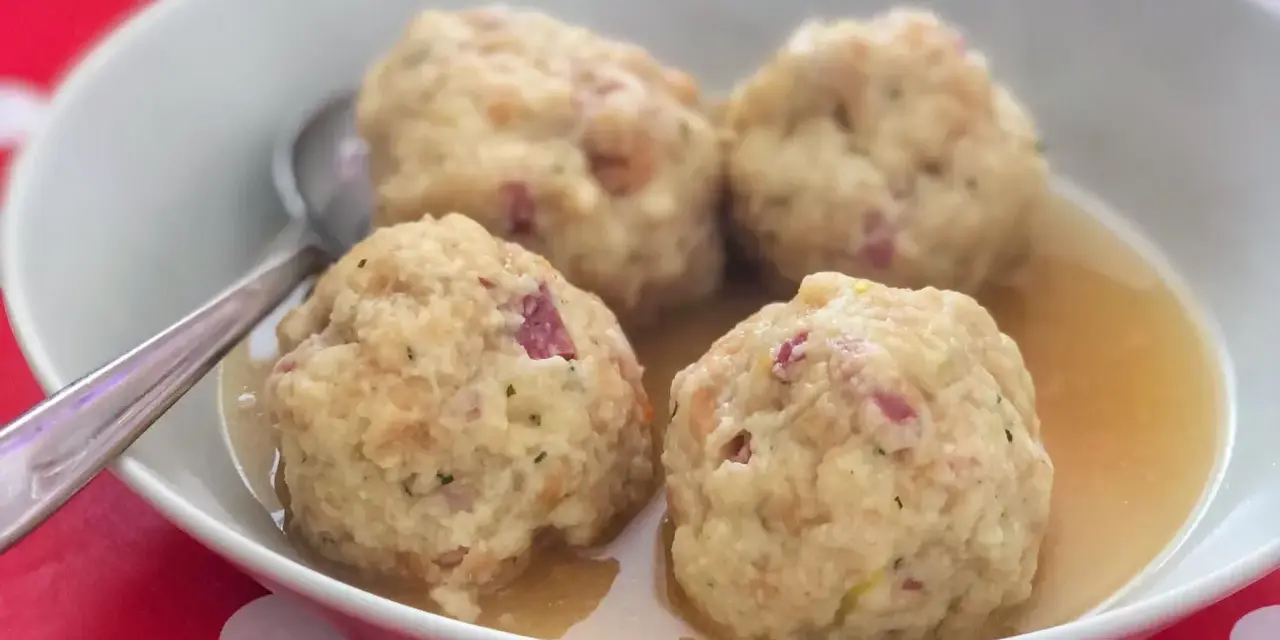 Canederli in brodo, un classico dei piatti tipici trentino alto adige, serviti in una ciotola bianca su un tovagliolo rosso a pois bianchi.