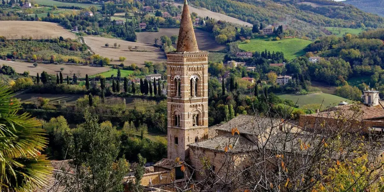 Campanile in borgo marchigiano, tra colline verdi e campi dorati, ideale per itinerari Marche autunnali.
