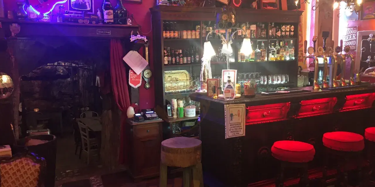 Interno della locanda del Principe a Artena, con chitarra elettrica luminosa, bancone bar e sgabelli rossi.