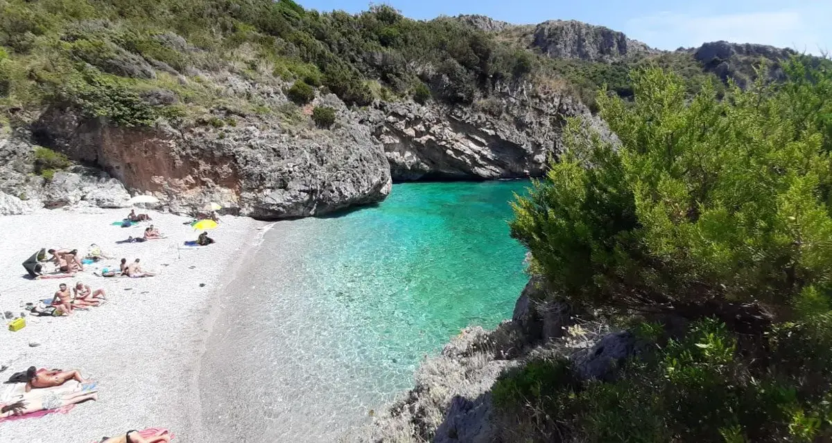 Spiaggia di ciottoli con gente che prende il sole e acque cristalline nel **Cilento mare**.