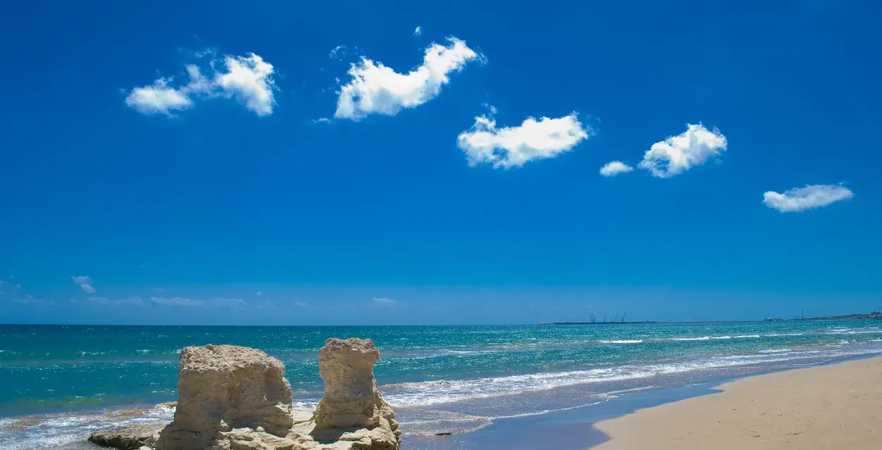 Spiagge bianche in Sicilia, con rocce scolpite dal mare e un cielo azzurro pieno di nuvole bianche.