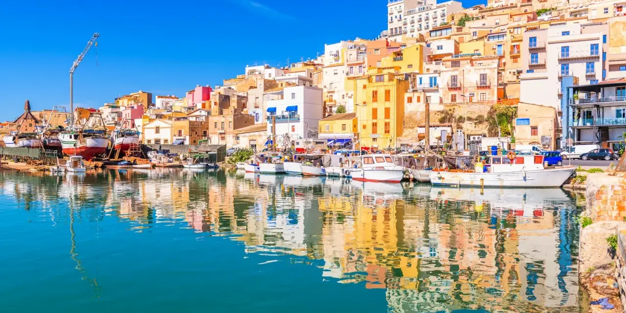 Porto di Sciacca: case colorate a picco sul mare, barche da pesca ormeggiate e riflessi sull'acqua. Un luogo incantevole da scoprire.