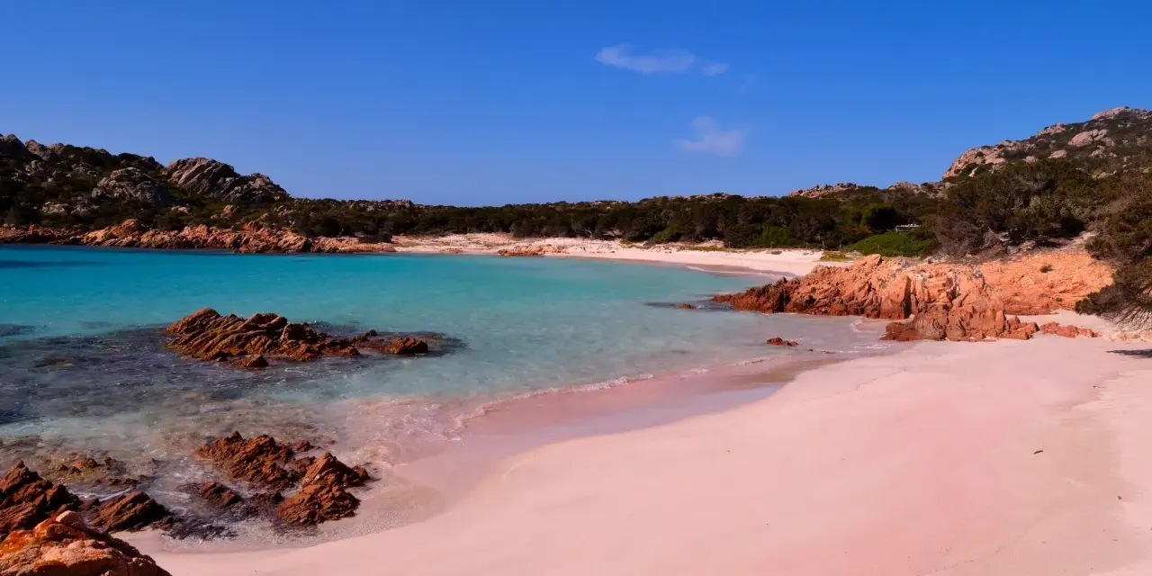 La **spiaggia rosa** di Asinara, con le sue acque turchesi e rocce rossastre, incanta sotto un cielo azzurro.