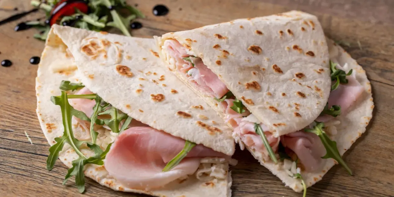 Piadina romagnola con prosciutto, rucola e formaggio. Un classico esempio di cosa si mangia in Emilia Romagna, semplice e gustosa.