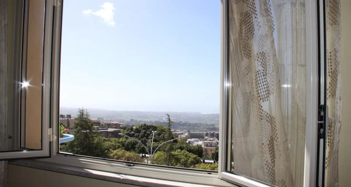 La terrazza sulla valle offre una vista panoramica su un paesaggio collinare con case e alberi verdi sotto un cielo azzurro.