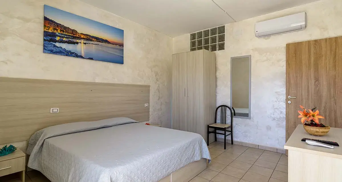 Camera accogliente all'Hotel Cristallo Paestum con letto matrimoniale, armadio, specchio e quadro con panorama marino.