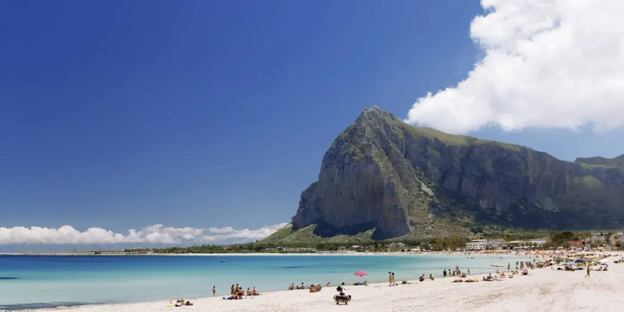Spiaggia di San Vito Lo Capo, Sicilia, con il Monte Monaco imponente sullo sfondo e il mare cristallino che invita a un bagno.