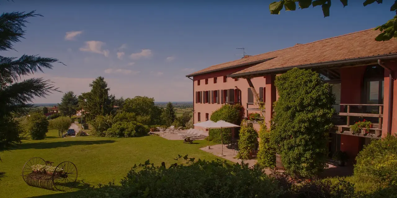 La casa rossa ai colli, immersa nel verde, offre un panorama incantevole. Un giardino curato con un antico attrezzo agricolo fiorito.